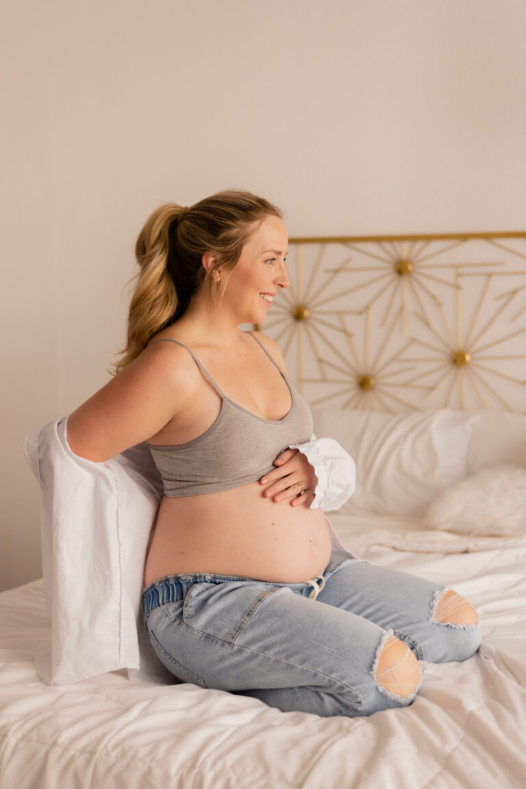 Pregnant mother holding her belly during maternity photography session on a bed wearing neutral minimal clothing