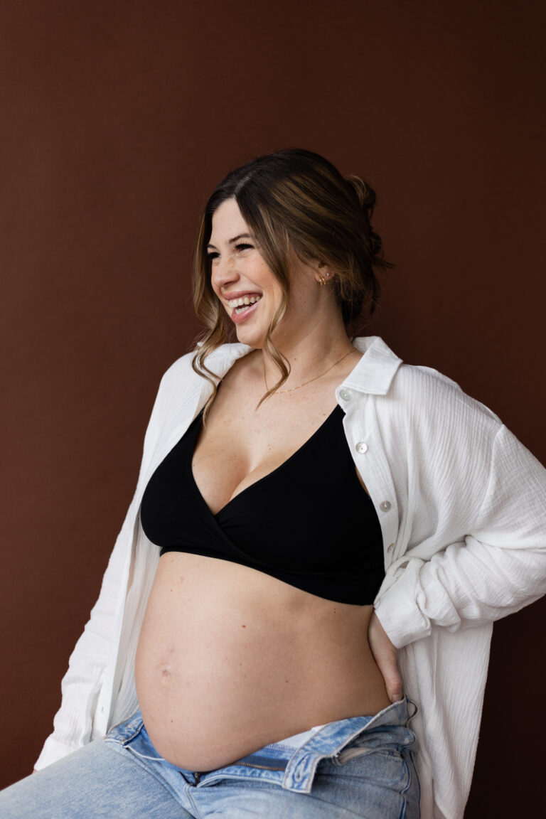 Expecting mother smiling while holding her pregnant belly for studio maternity photography session