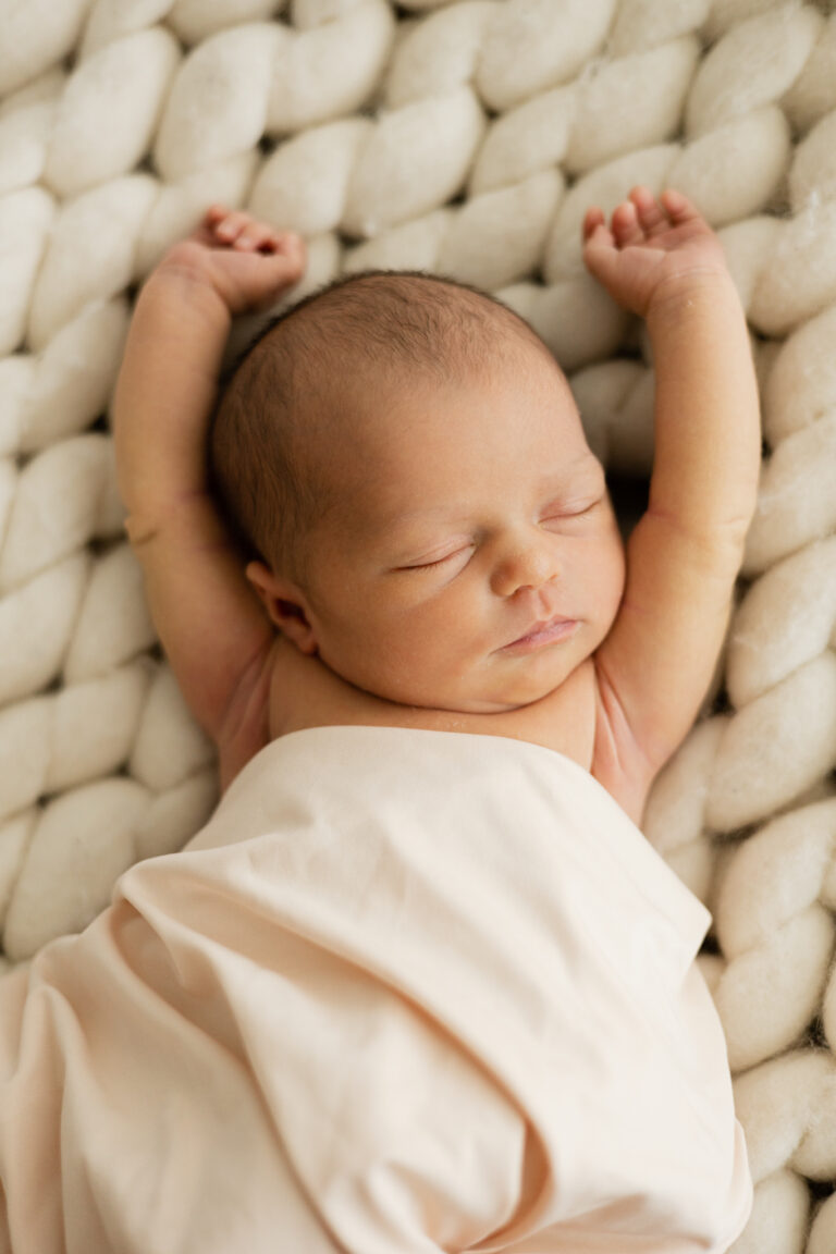 Newborn baby girl laying on her back with her arms above her head sleeping for a newborn photography session