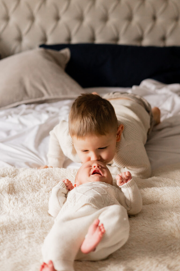 Toddler boy kisses newborn baby brother on their bed in Lake Stevens Washington for in home newborn session