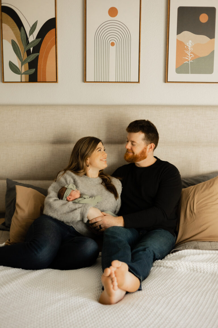 A husband and wife cuddling in their bed holding their newborn baby girl during their in home newborn photography session