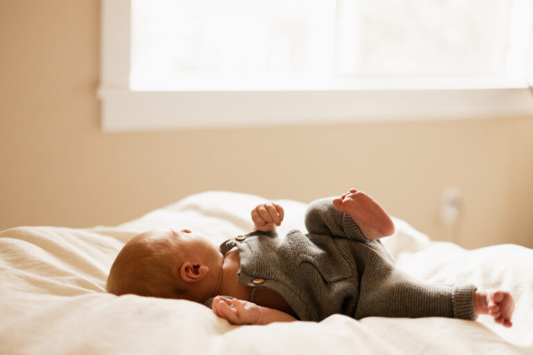 professional photography picture of newborn baby boy on a bed in front of a window during a newborn session