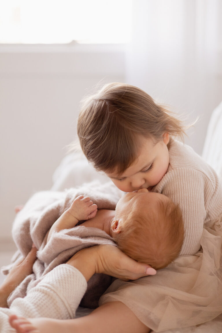 Toddler holds and kisses newborn baby sibling at studio photoshoot in Seattle