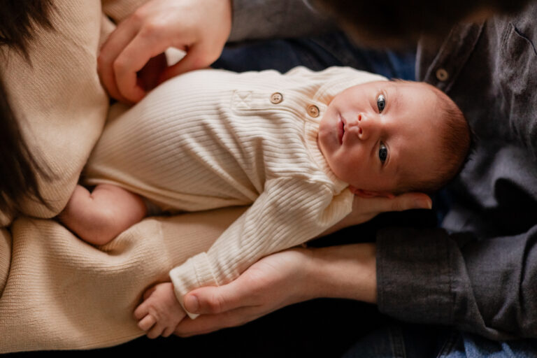 Baby being held by parents looks up at camera during in home newborn session in Seattle, WA