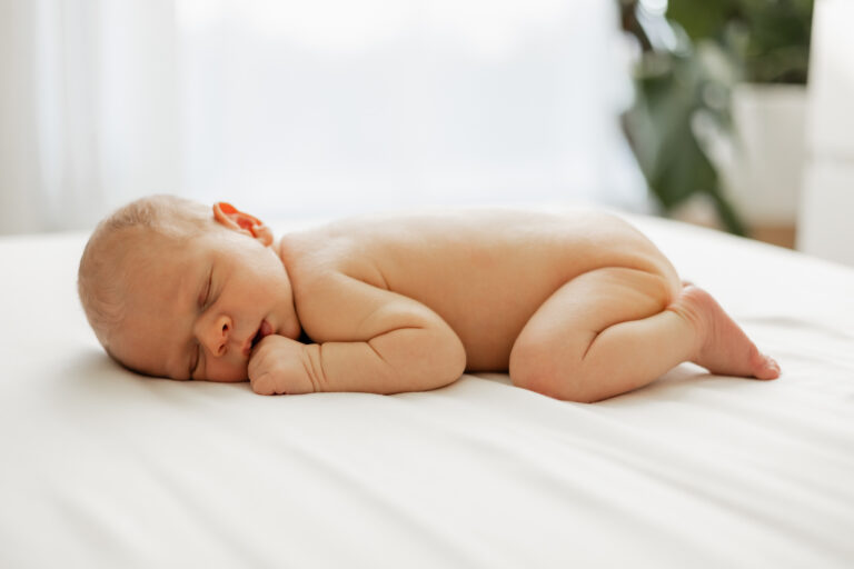 Naked baby sleeping on bed during in home newborn session in Seattle, WA
