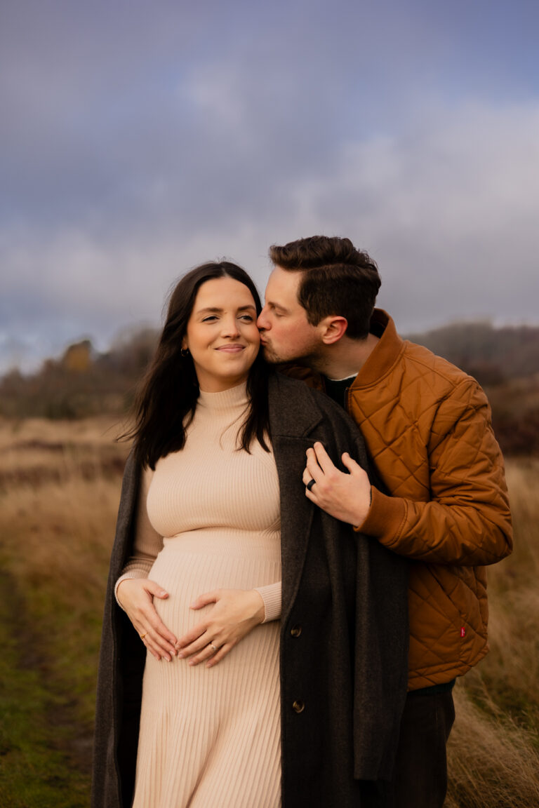 couple kissing while holding pregnant belly for Seattle outdoor maternity session