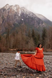 Son holds pregnant moms dress for her while they walk along the river in North Bend, WA during maternity photo session