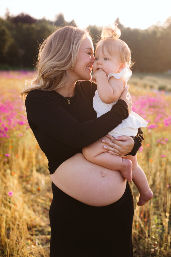 Pregnant mom holds toddler baby in a field full of flowers in Woodinville for maternity photoshoot