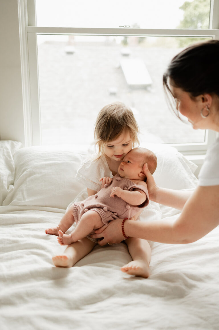 Toddler holding newborn baby sister in bed during photoshoot
