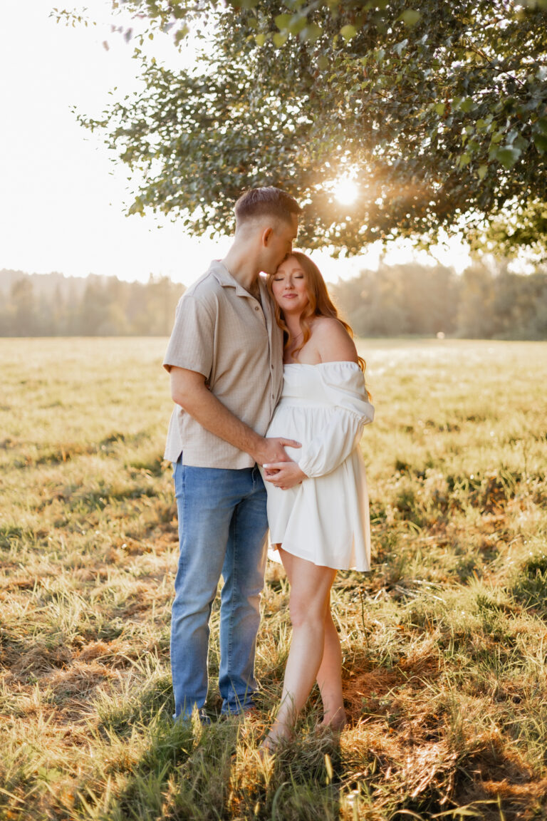 Expecting mom and dad hugging and kissing under a tree in North Bend Field with the sun setting behind them for maternity photoshoot