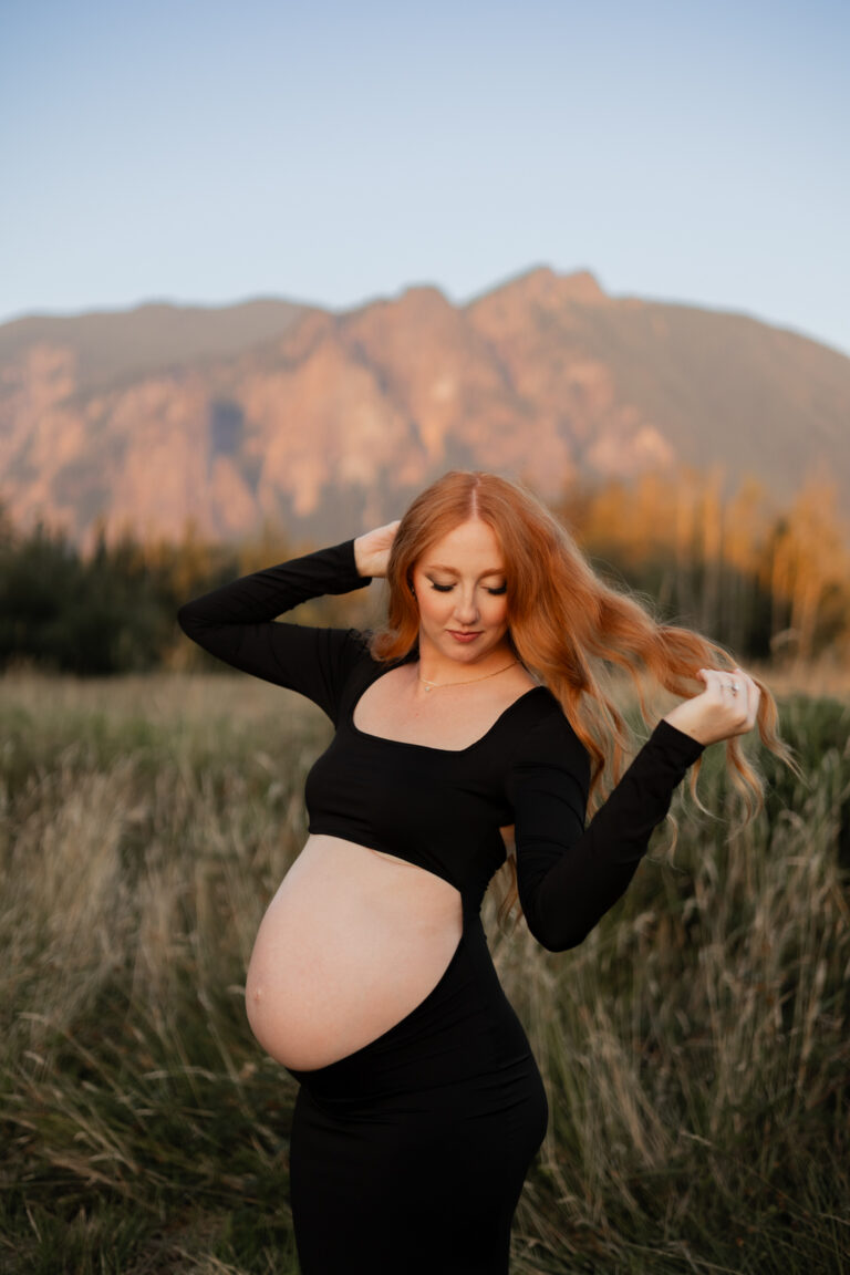 pregnant mom playing with her hair in North Bend field with Mt. Si in the background during sunset for maternity session
