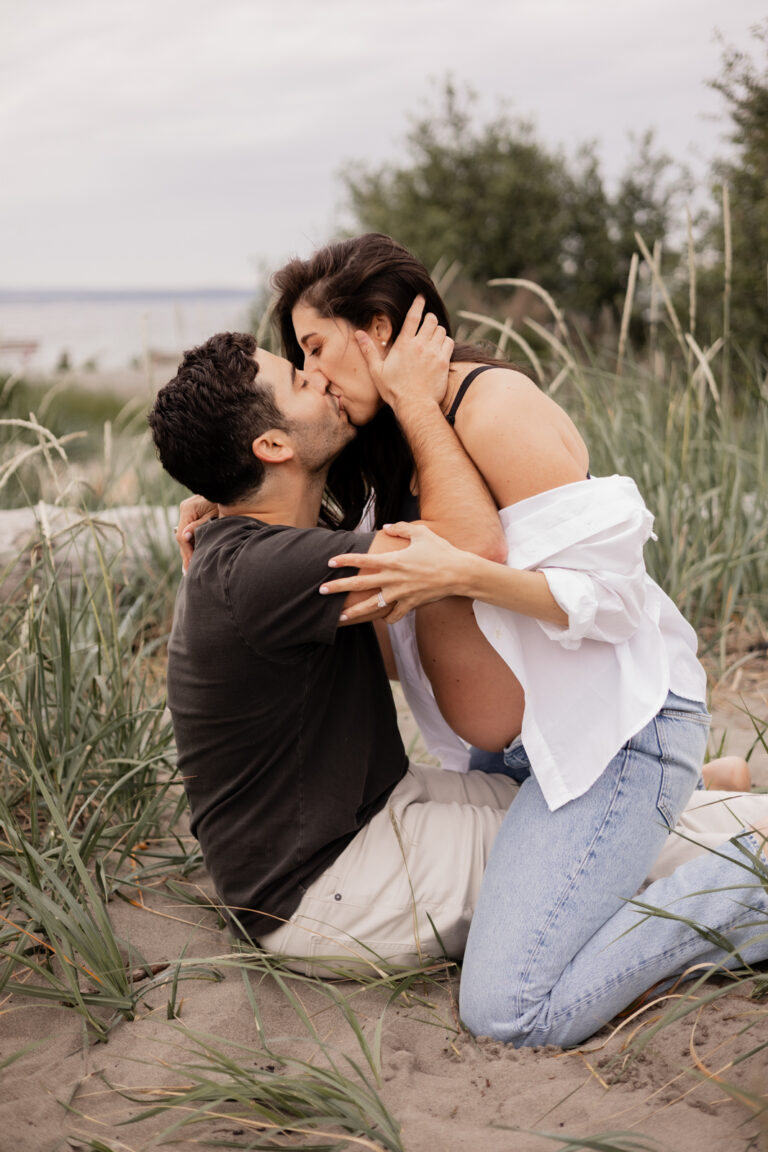 Expecting mom kisses husband romantically on Golden Gardens beach during maternity photoshoot