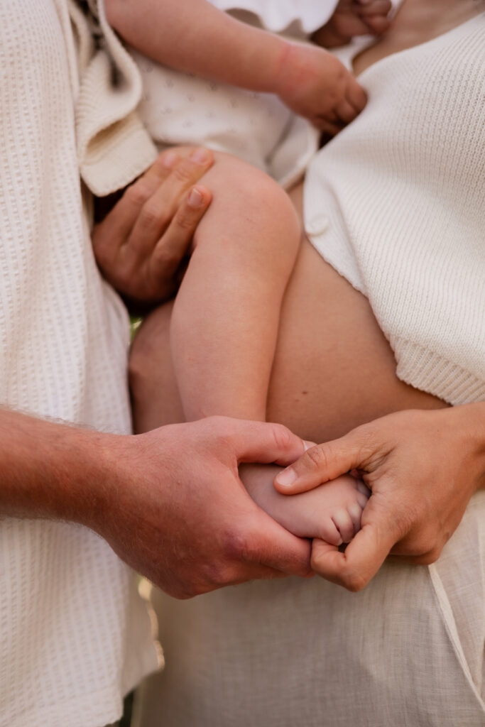 Image on pregnant belly holding toddler with parents hands on their babies foot during family maternity session