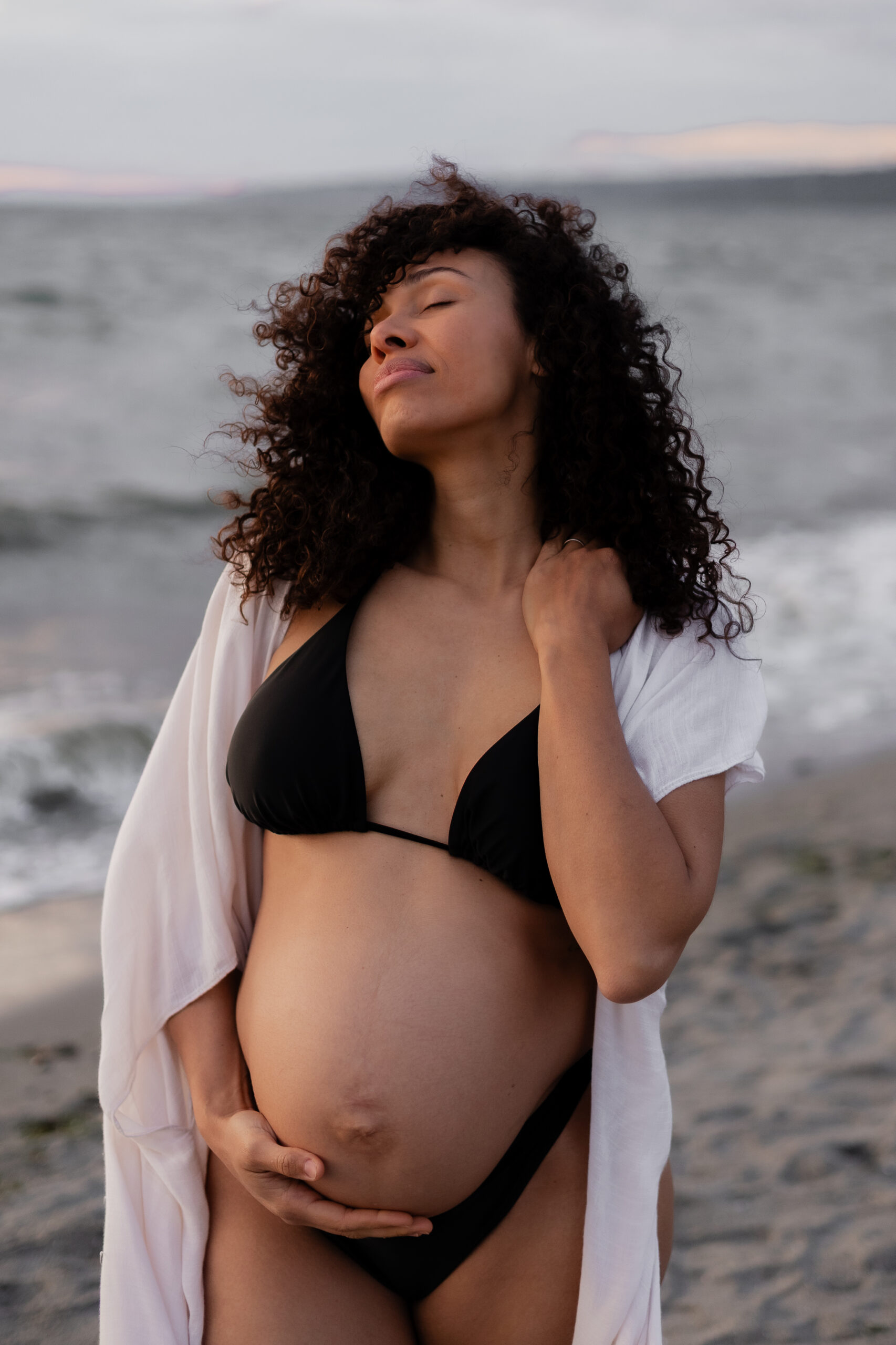 Pregnant woman posing for Seattle maternity photographer on the beach during sunset