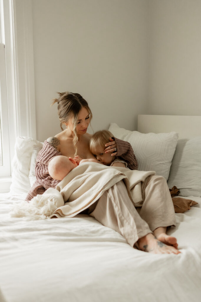 Mom tandem breastfeeds newborn baby and toddler during in home photoshoot in Seattle