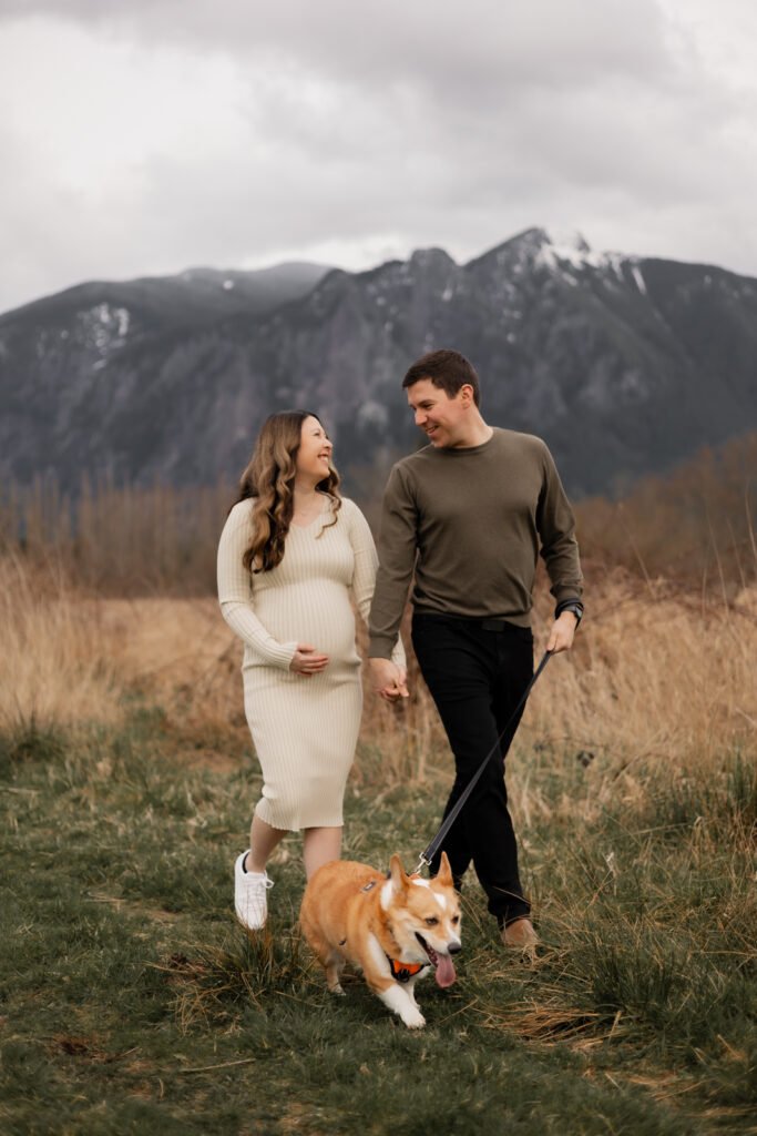 Pregnant couple and their dog walk together holding hands during maternity photos