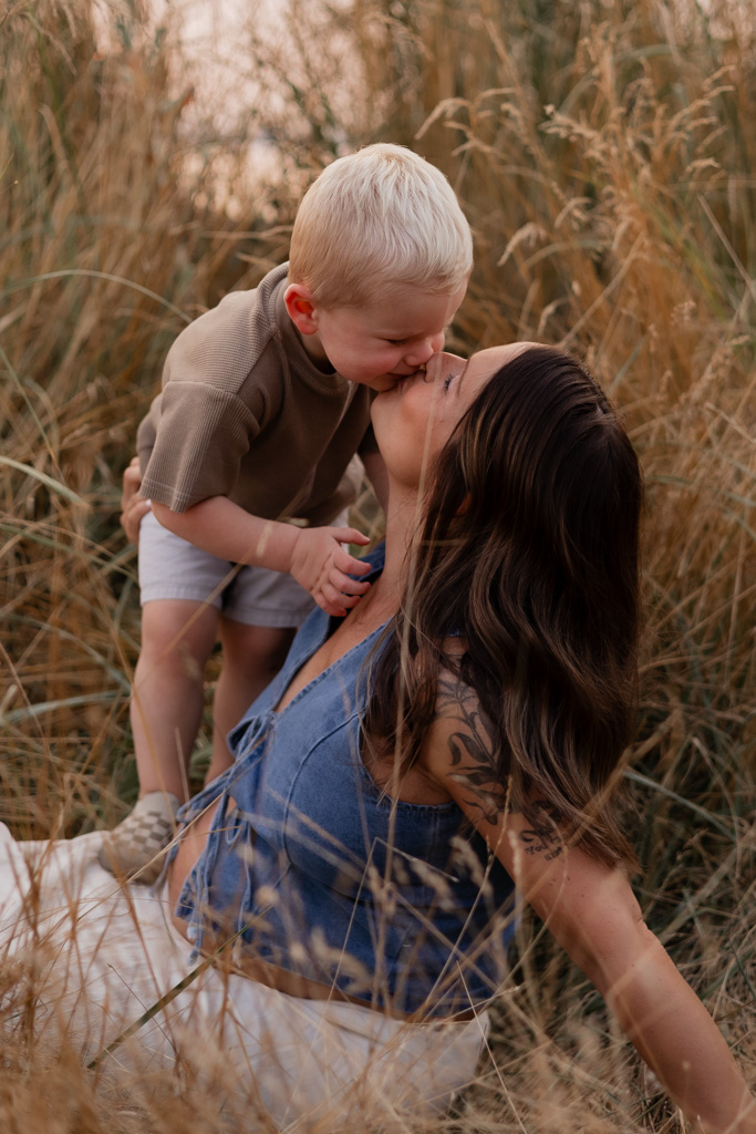 maternity photoshoot at golden gardens beach park in Seattle with a pregnant mom kissing her toddler son