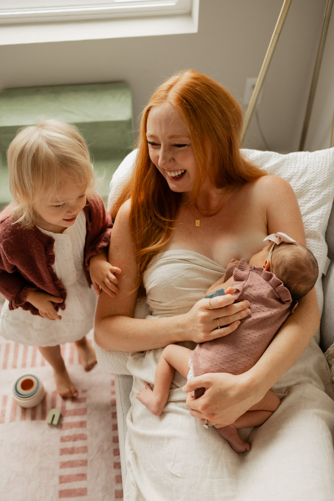 Mother breastfeeding her newborn baby while laughing at her toddler during an in-home photoshoot in Snohomish, WA